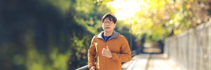 Man in orange jacket and glasses running along path