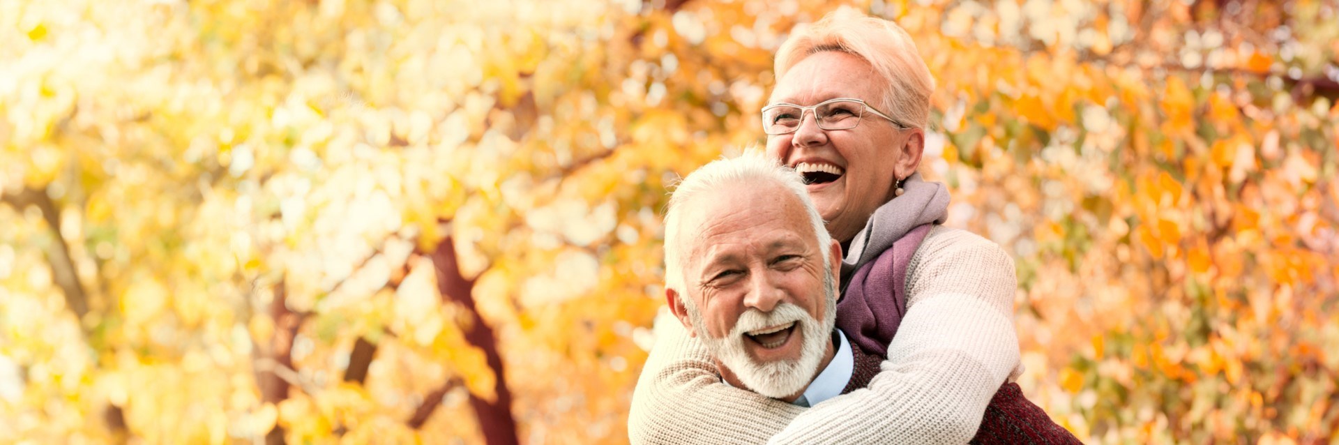 Older couple laughing in front of autumn trees