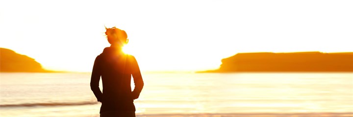 Woman looking out to sea on beach at sunset