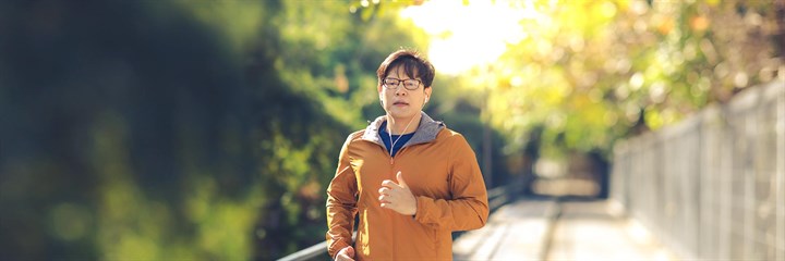 Man in orange jacket and glasses running along path