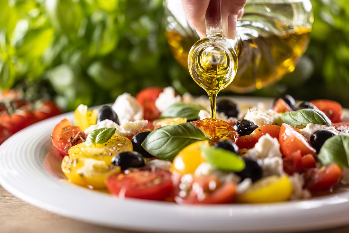 Olive oil being poured onto a Mediterranean salad